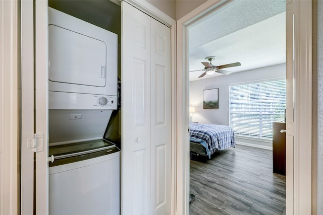 clothes washing area with stacked washer and dryer, ceiling fan, baseboards, wood finished floors, and laundry area