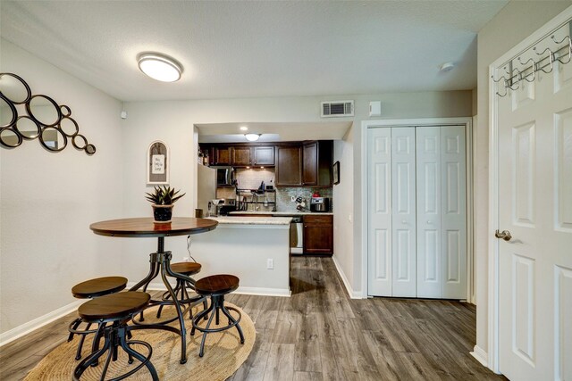 kitchen with dark wood-style floors, decorative backsplash, dark brown cabinetry, visible vents, and a peninsula