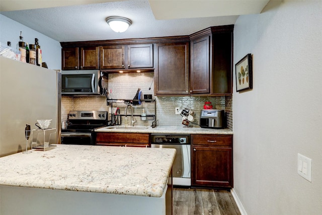 kitchen with a sink, stainless steel appliances, dark brown cabinetry, backsplash, and wood finished floors
