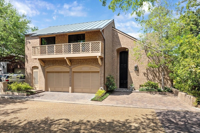 view of front of home with a standing seam roof, a garage, brick siding, decorative driveway, and a balcony