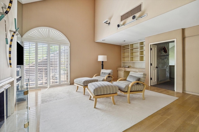 sitting room with built in features, a towering ceiling, wood finished floors, and a premium fireplace