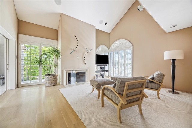 living room featuring high vaulted ceiling, a glass covered fireplace, and wood finished floors