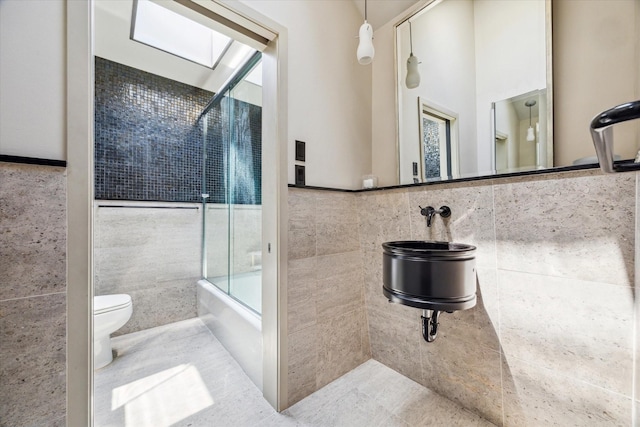 full bath with a skylight, tile walls, wainscoting, toilet, and enclosed tub / shower combo