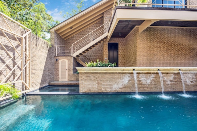 rear view of house featuring brick siding, an in ground hot tub, and a balcony