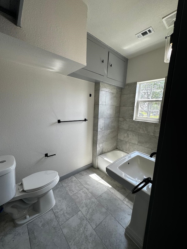 3401 Illinois St, Baytown, TX 77520 - bathroom with a washtub, a textured ceiling, baseboards, toilet, and visible vents