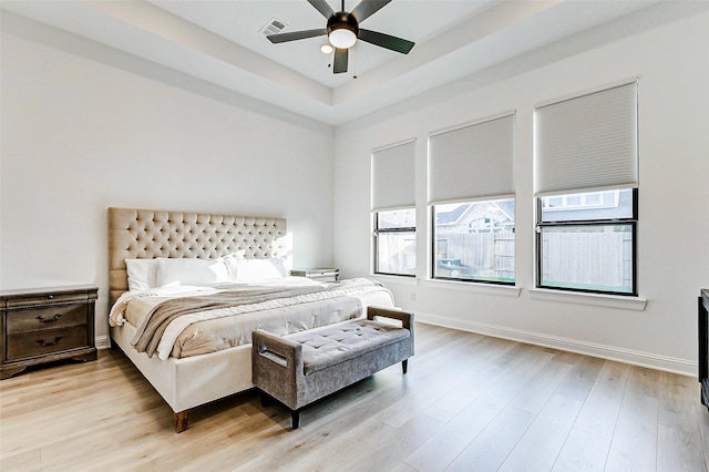 bedroom featuring ceiling fan, a raised ceiling, baseboards, light wood-type flooring, and visible vents