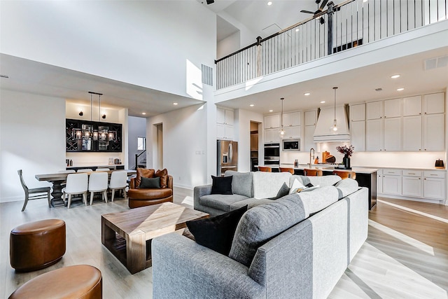 living room with light wood-style floors, a high ceiling, a chandelier, and visible vents