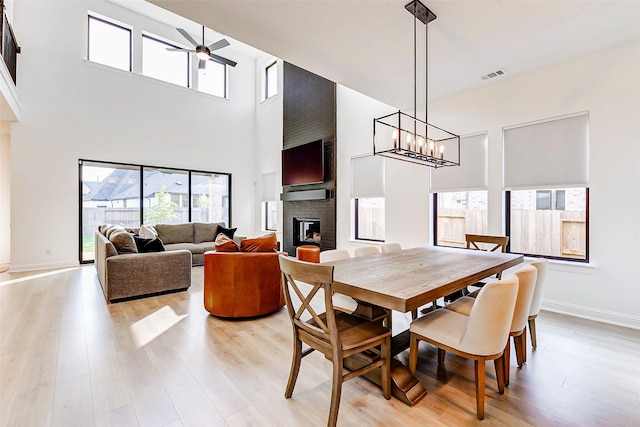 dining space featuring a brick fireplace, visible vents, a healthy amount of sunlight, and ceiling fan with notable chandelier
