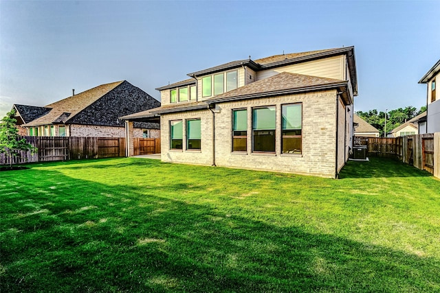 rear view of house with a yard, brick siding, a fenced backyard, and roof with shingles