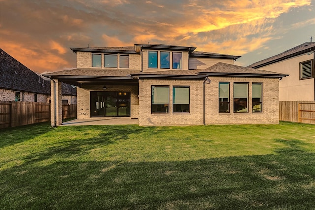 back of house featuring a fenced backyard, a patio, a lawn, and brick siding