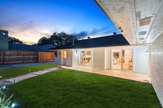 back of property at dusk featuring a wooden deck, a yard, brick siding, and fence