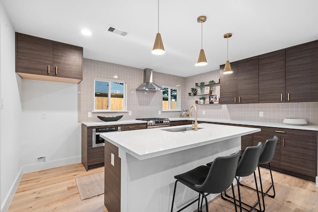 kitchen featuring tasteful backsplash, wall chimney exhaust hood, light wood-type flooring, and a sink