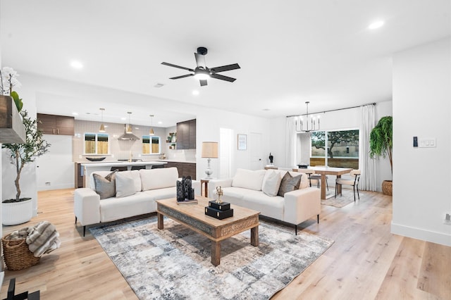 living area with ceiling fan with notable chandelier, baseboards, recessed lighting, and light wood finished floors