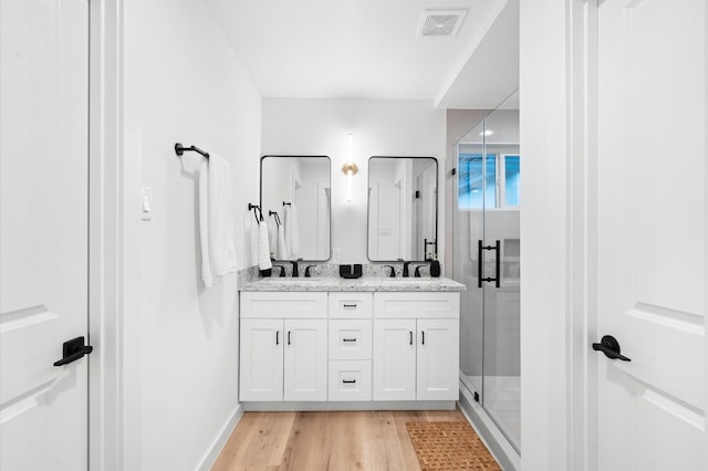 full bathroom with a sink, wood finished floors, a stall shower, double vanity, and visible vents