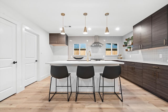 kitchen featuring a breakfast bar, tasteful backsplash, wall chimney range hood, and open shelves