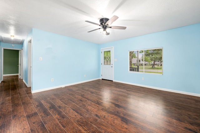unfurnished room with baseboards, ceiling fan, attic access, and dark wood-style flooring