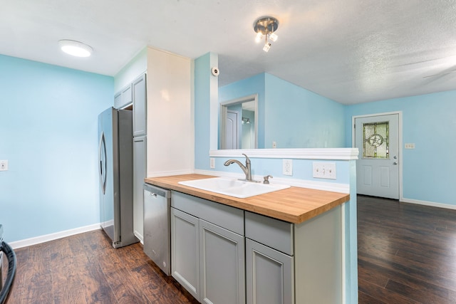 kitchen featuring a sink, butcher block countertops, dark wood finished floors, stainless steel appliances, and a peninsula