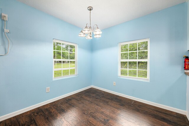 spare room with baseboards, dark wood-style flooring, and a notable chandelier