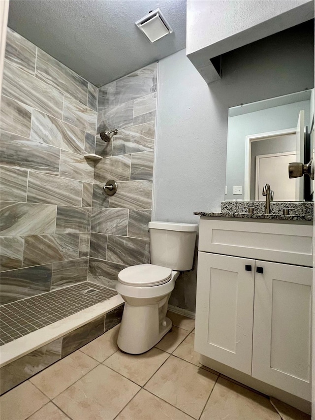 bathroom featuring tile patterned floors, a tile shower, toilet, visible vents, and vanity
