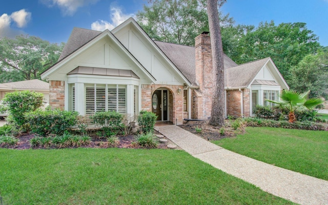 view of front of house featuring board and batten siding, a chimney, a front yard, brick siding, and a shingled roof