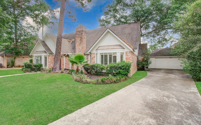 tudor house featuring a front yard, roof with shingles, a chimney, brick siding, and driveway