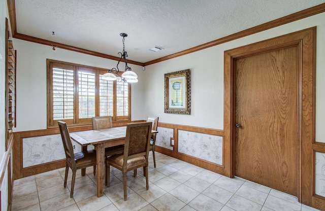 dining room with an inviting chandelier, a wainscoted wall, ornamental molding, and a textured ceiling