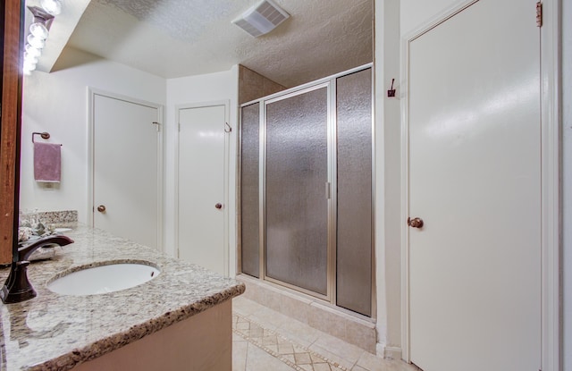 full bath featuring a textured ceiling, visible vents, tile patterned flooring, a shower stall, and a sink