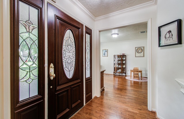entrance foyer with a textured ceiling, visible vents, baseboards, light wood finished floors, and ornamental molding