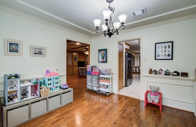 game room with visible vents, ornamental molding, an inviting chandelier, wood finished floors, and a textured ceiling
