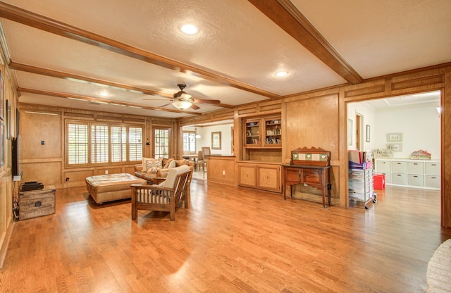 living room featuring wood walls, beamed ceiling, ceiling fan, a textured ceiling, and light wood finished floors