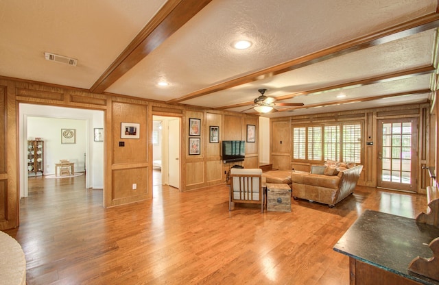 living area with visible vents, beamed ceiling, ceiling fan, a textured ceiling, and light wood-style flooring