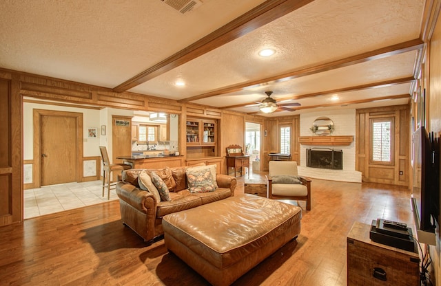living area featuring a textured ceiling, visible vents, light wood-type flooring, and a decorative wall