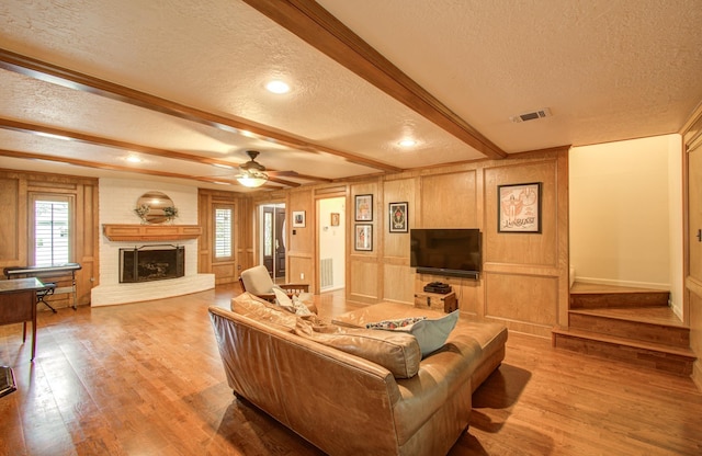 living area with a brick fireplace, a textured ceiling, visible vents, and light wood-style floors