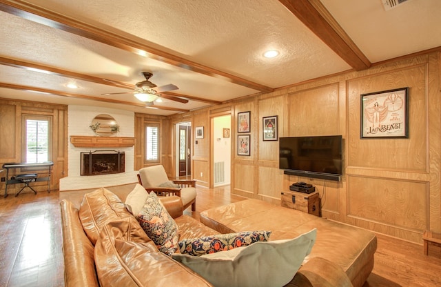 living area featuring wood finished floors, a textured ceiling, a brick fireplace, and beam ceiling