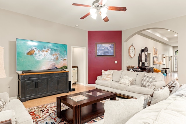 living room featuring light tile patterned flooring, arched walkways, ceiling fan, and baseboards