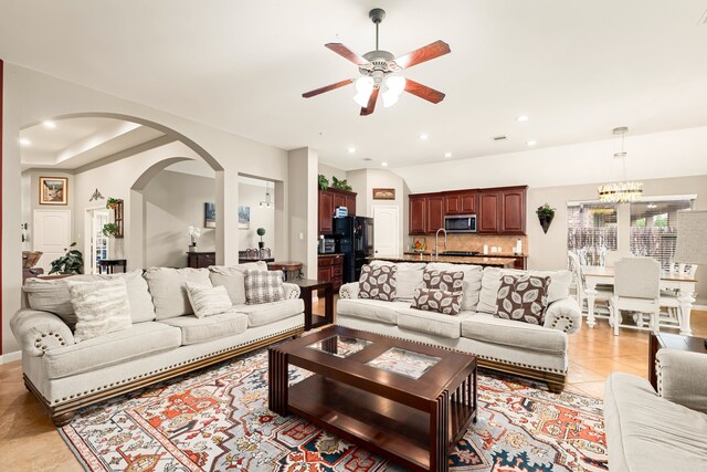 living area featuring light tile patterned floors, recessed lighting, arched walkways, and ceiling fan with notable chandelier