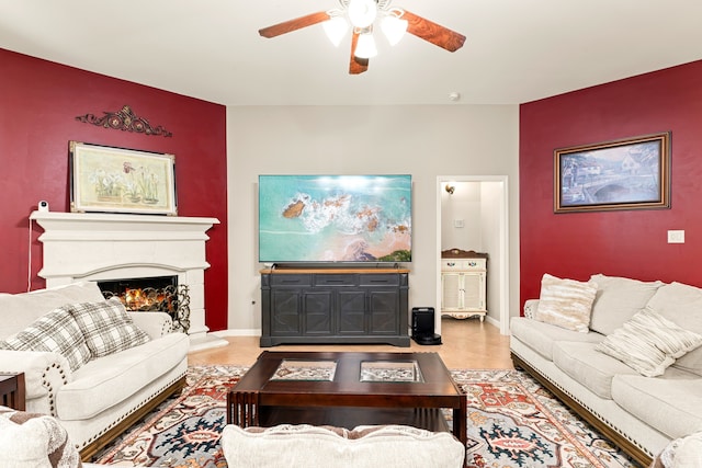 living room with tile patterned floors, a ceiling fan, a lit fireplace, baseboards, and an accent wall