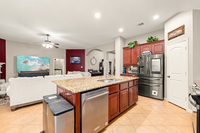 kitchen featuring arched walkways, light tile patterned floors, stainless steel appliances, a sink, and a center island with sink