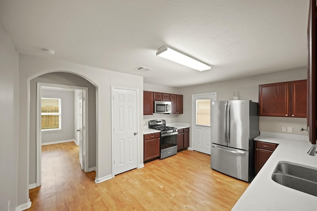 kitchen featuring light wood finished floors, stainless steel appliances, a sink, visible vents, and light countertops