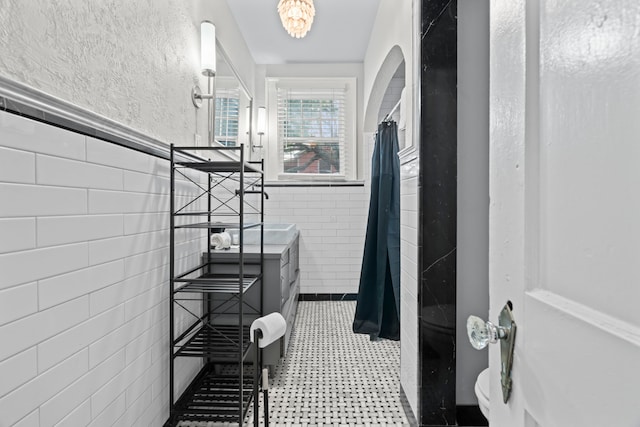 bathroom featuring tile patterned floors, a wainscoted wall, a shower with curtain, tile walls, and a notable chandelier