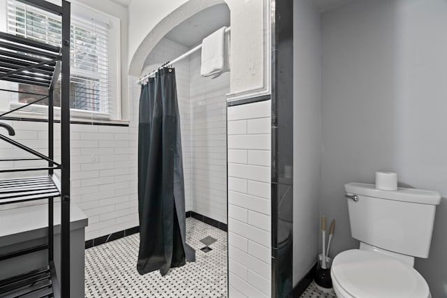 bathroom with a tile shower, toilet, and tile walls