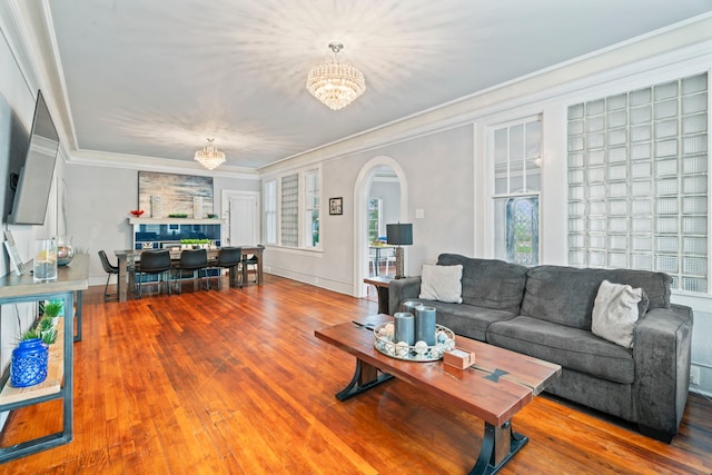 living area featuring arched walkways, wood finished floors, an inviting chandelier, and ornamental molding