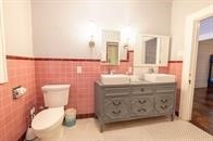 bathroom featuring double vanity, toilet, wainscoting, tile walls, and crown molding