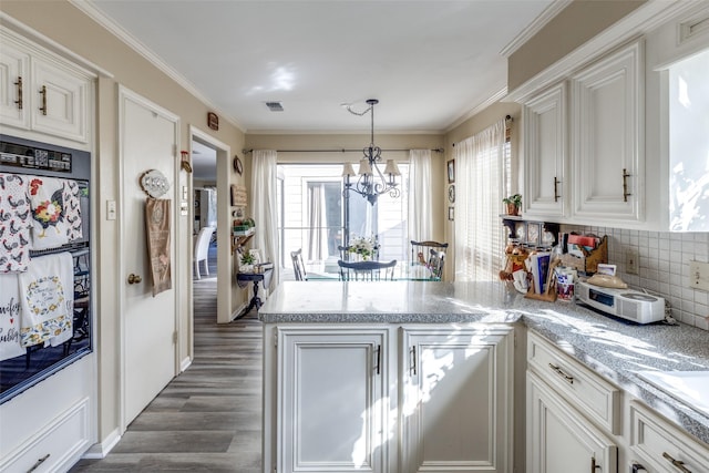 kitchen featuring a peninsula, dark wood finished floors, visible vents, backsplash, and a chandelier