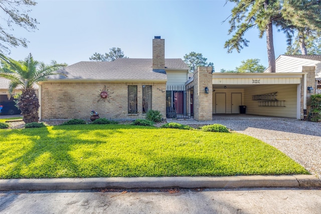 single story home featuring a chimney, driveway, a carport, brick siding, and a front yard