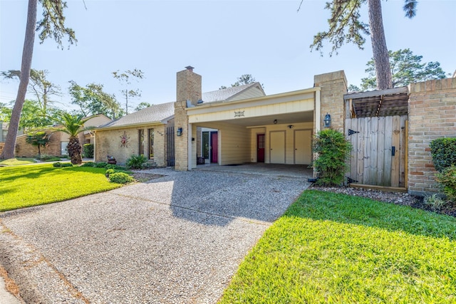 ranch-style home with an attached carport, a chimney, brick siding, a front yard, and aphalt driveway