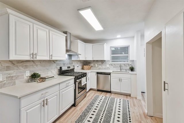 105 E Wavy Oak Cir, The Woodlands, TX 77381 - kitchen featuring appliances with stainless steel finishes, wall chimney range hood, a sink, white cabinetry, and light wood-type flooring