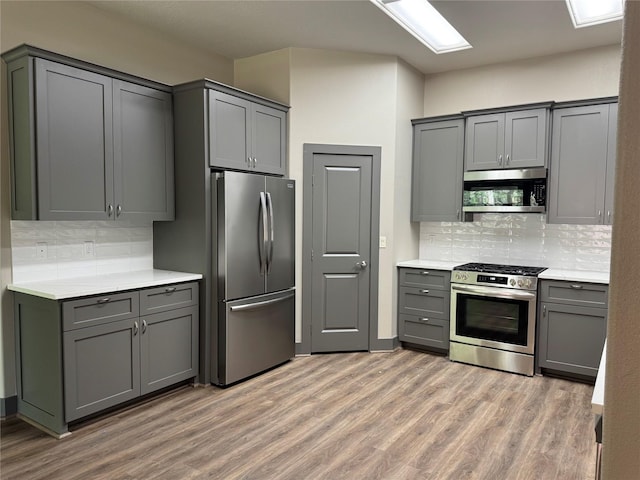 250 Bucek Ln, Schulenburg, TX 78956 - kitchen featuring tasteful backsplash, gray cabinets, light wood-type flooring, light countertops, and appliances with stainless steel finishes