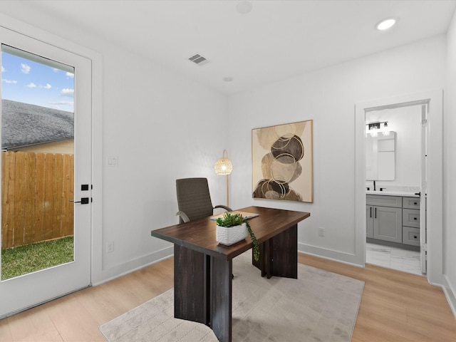 office space featuring baseboards, light wood-style floors, visible vents, and a sink