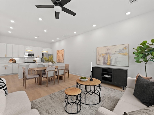 living room with a ceiling fan, light wood finished floors, baseboards, visible vents, and recessed lighting